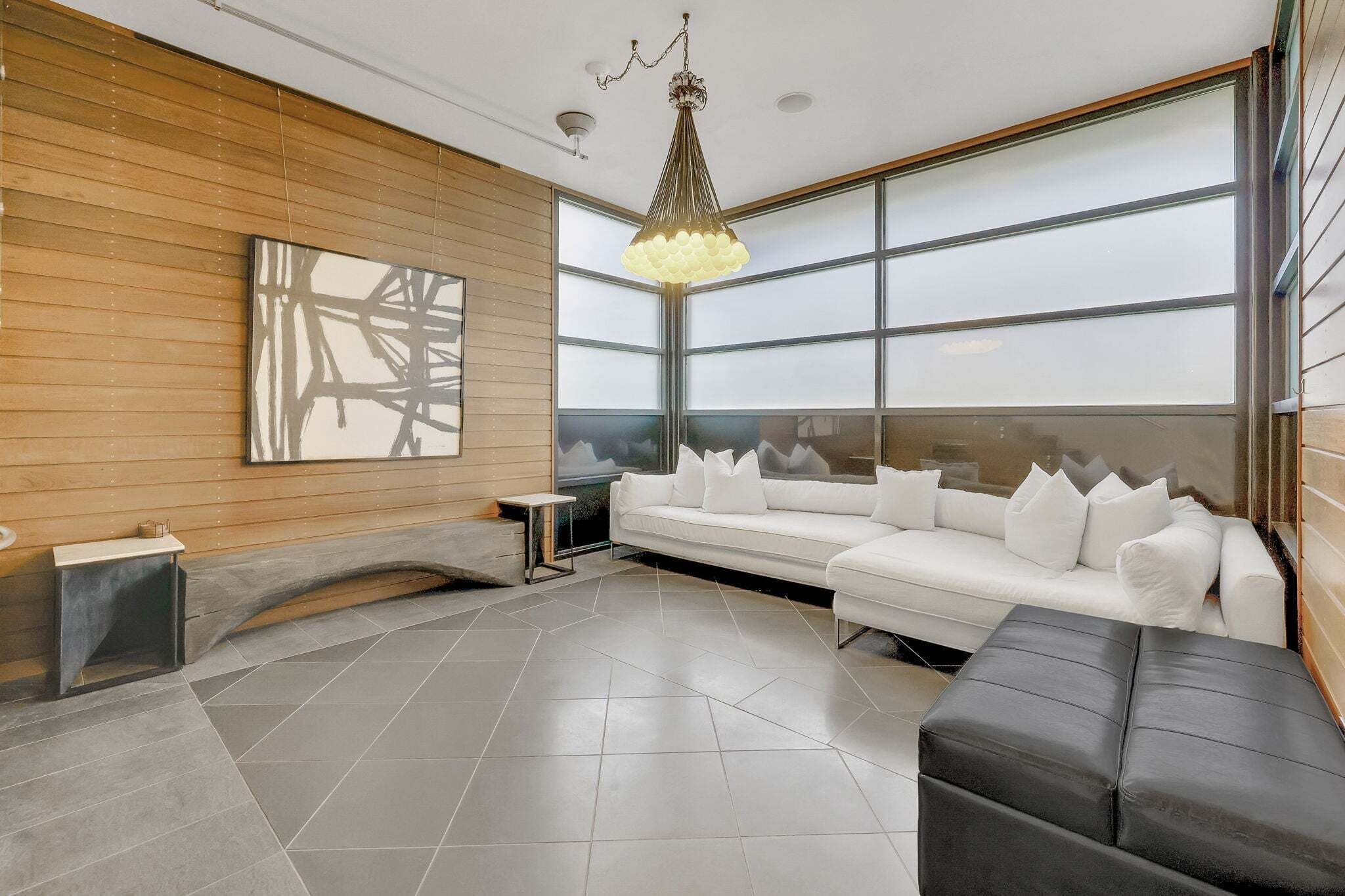 A modern interior with a white sofa, a black ottoman, a large abstract painting, and a unique ceiling light fixture.