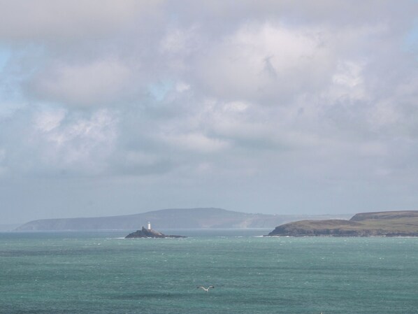 A lighthouse on a small island in the sea with a cloudy sky.