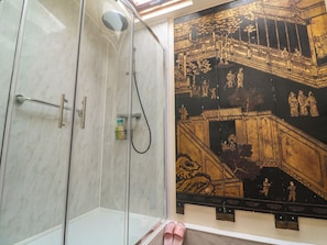 Un baño con cabina de ducha de vidrio, un panel decorativo en la pared y un par de pantuflas rosas en el suelo.