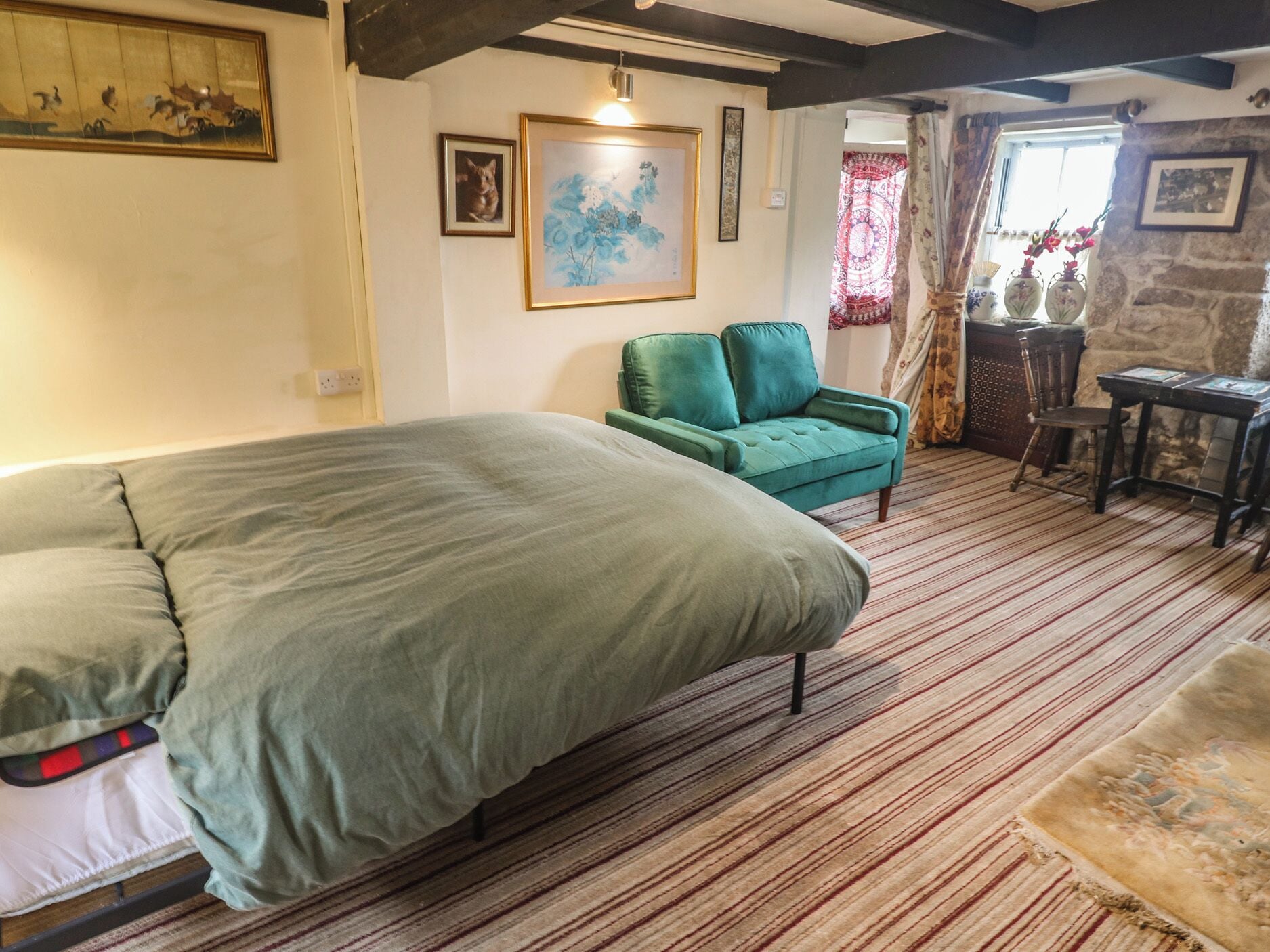 A room with a bed, a green sofa, a table with chairs, and a stone wall.