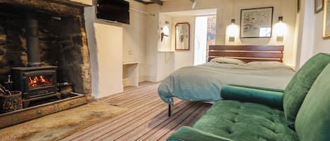 A room with a fireplace, a bed, a green sofa, and a television mounted on the wall.
