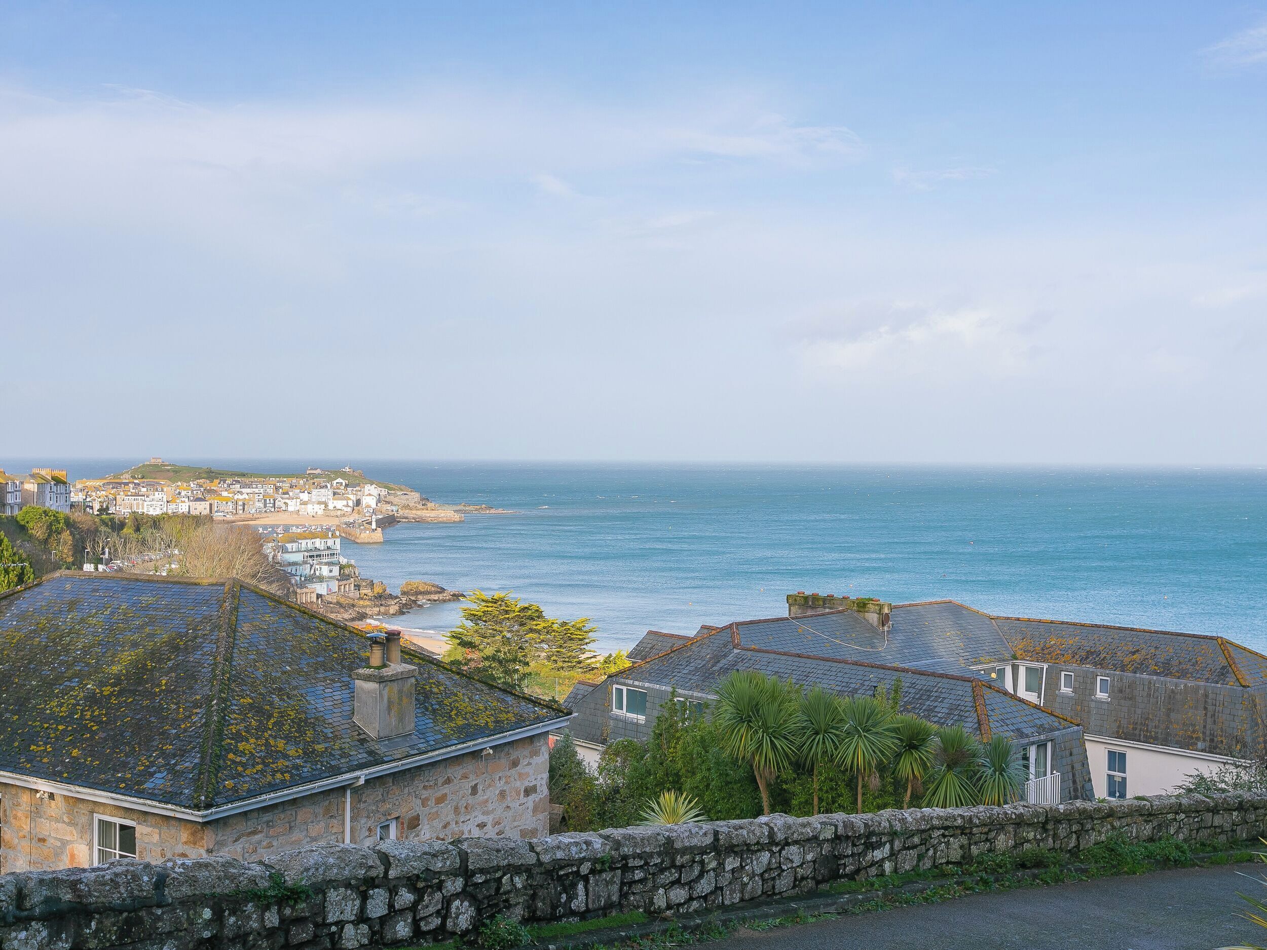 A coastal town with stone buildings, a stone wall, and a view of the sea.
