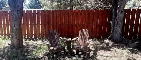 A fenced backyard with two wooden chairs and a small table.