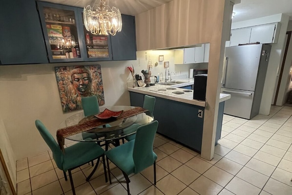Una cocina moderna con comedor, que incluye una araña, un refrigerador y un cuadro en la pared.