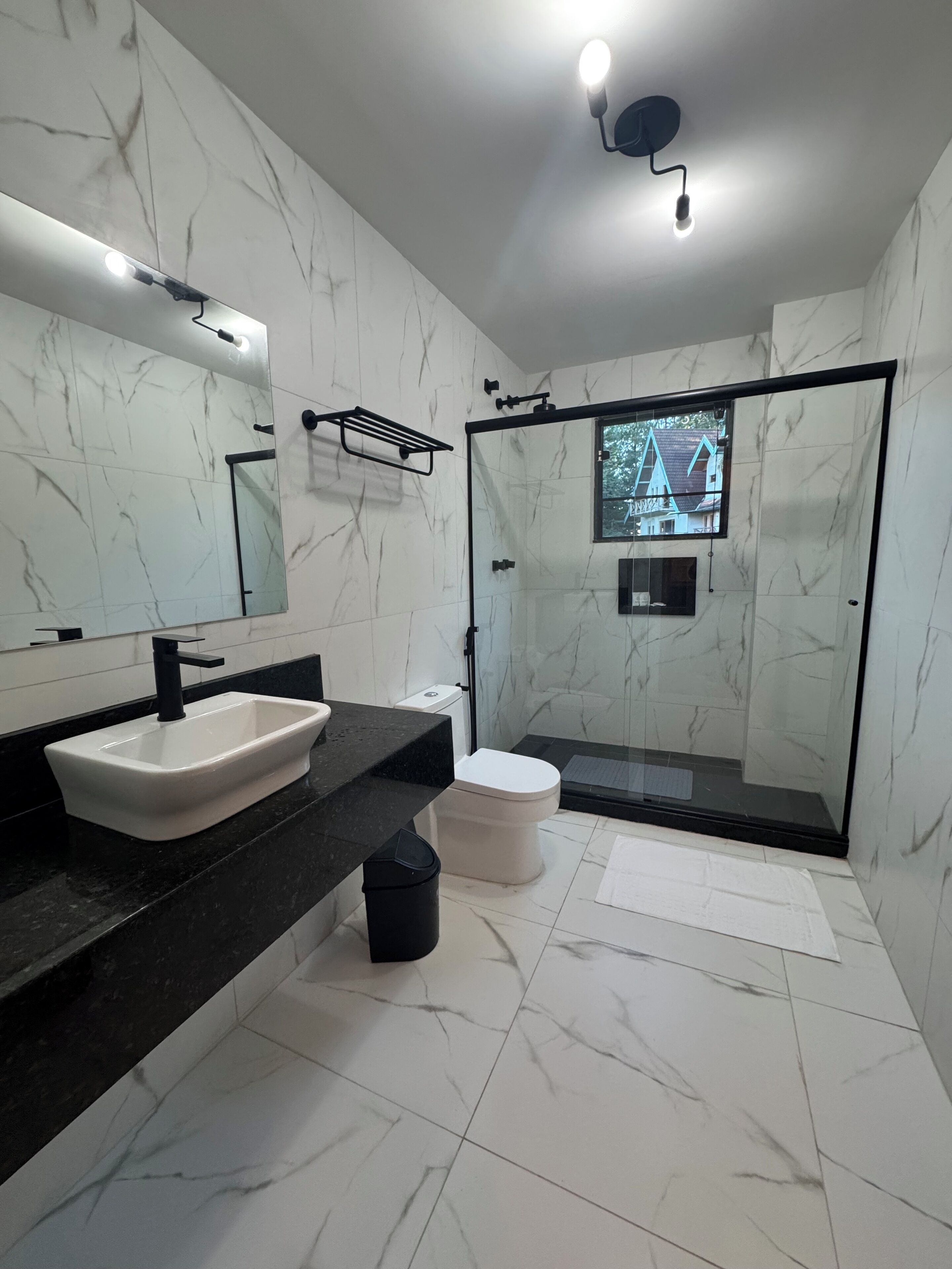 A modern bathroom with a white marble vanity, a black sink, a toilet, and a glass-enclosed shower.