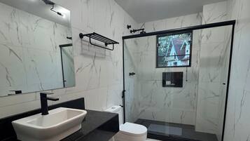A modern bathroom with a white marble vanity, a black sink, a toilet, and a glass-enclosed shower.