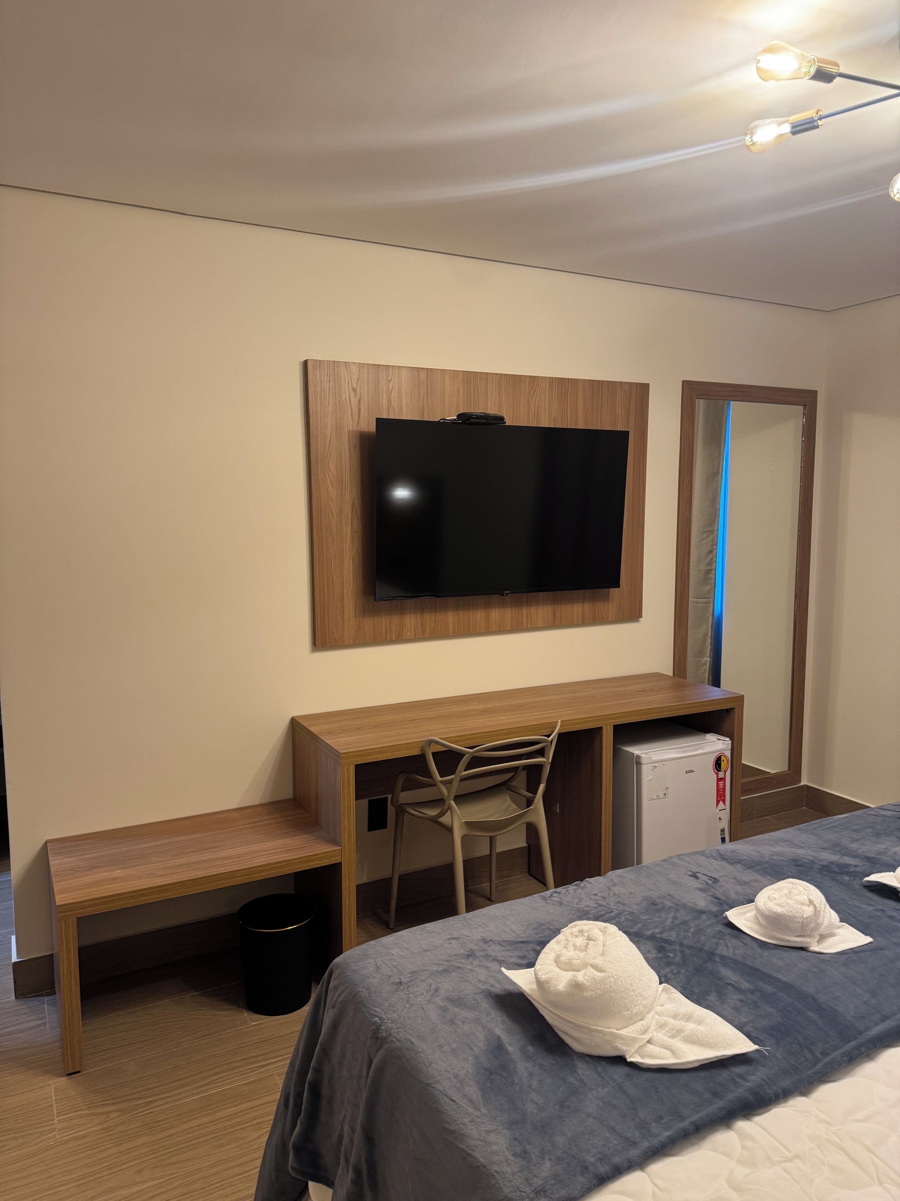 Une chambre d’hôtel comprenant un lit, un bureau avec une chaise, un téléviseur fixé au mur et un petit réfrigérateur.