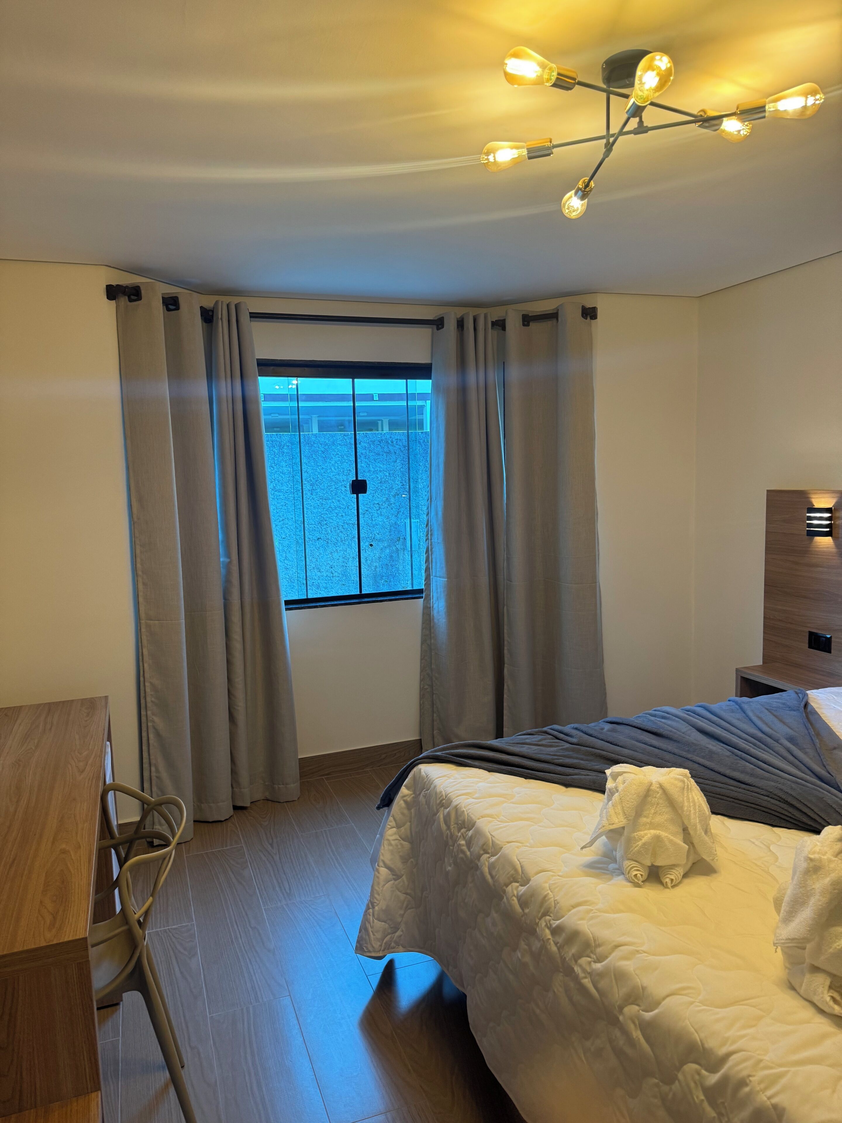 Ein Hotelzimmer mit einem Bett, einem Schreibtisch, einem Stuhl und einem fensterbepflanzten Fenster.
