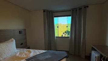 Habitación de hotel con cama, escritorio, ventana con cortinas y vista a zonas verdes.
