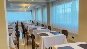 Un salón de banquetes con filas de mesas y sillas, ventanas amplias y una moderna lámpara de araña.