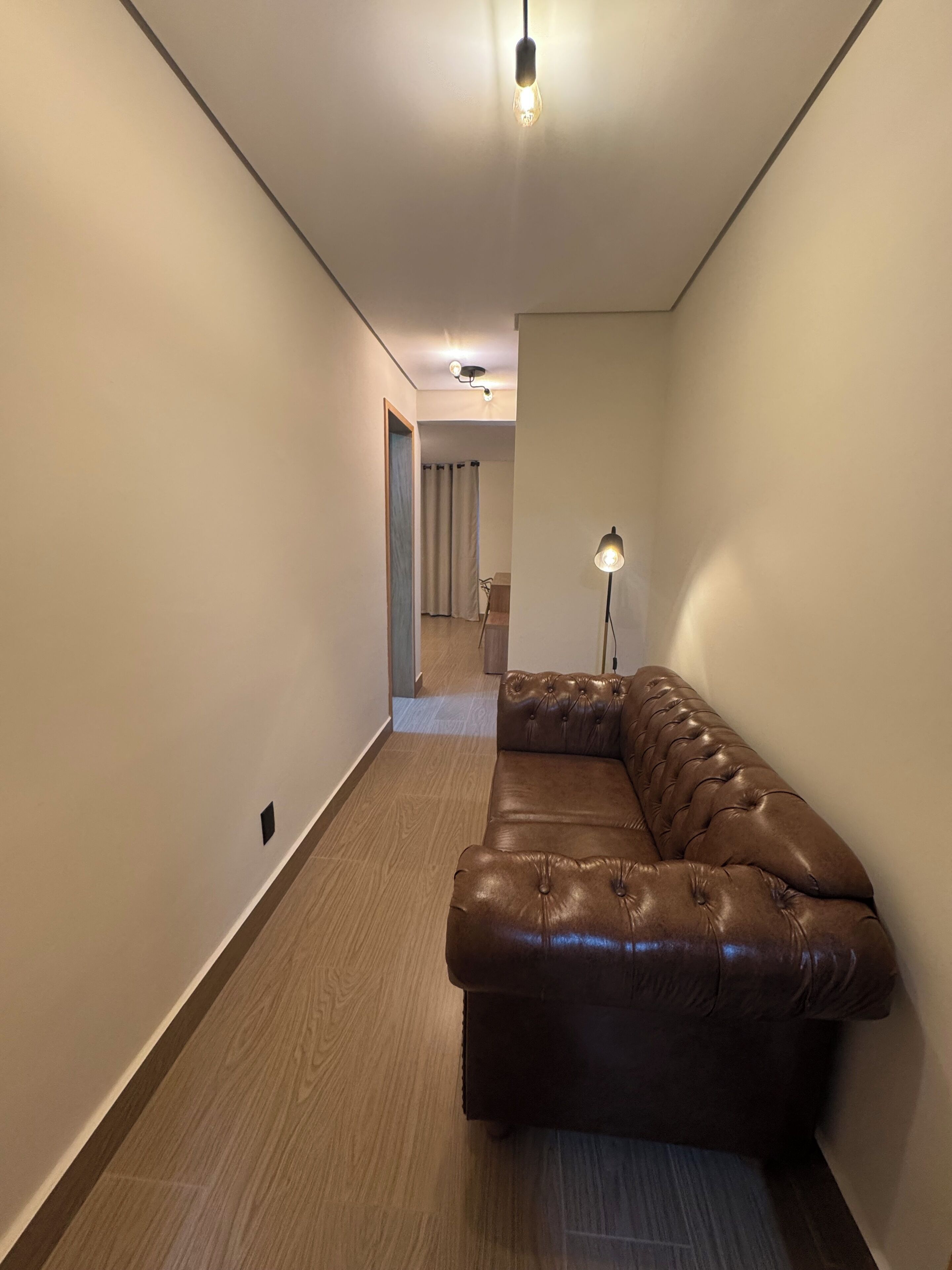 A modern living room with a leather sofa, a floor lamp, and a hallway leading to another room.