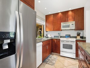 A modern kitchen with stainless steel appliances, wooden cabinets, and a granite countertop. - Wailea Ekahi Village 20D (Wailea)