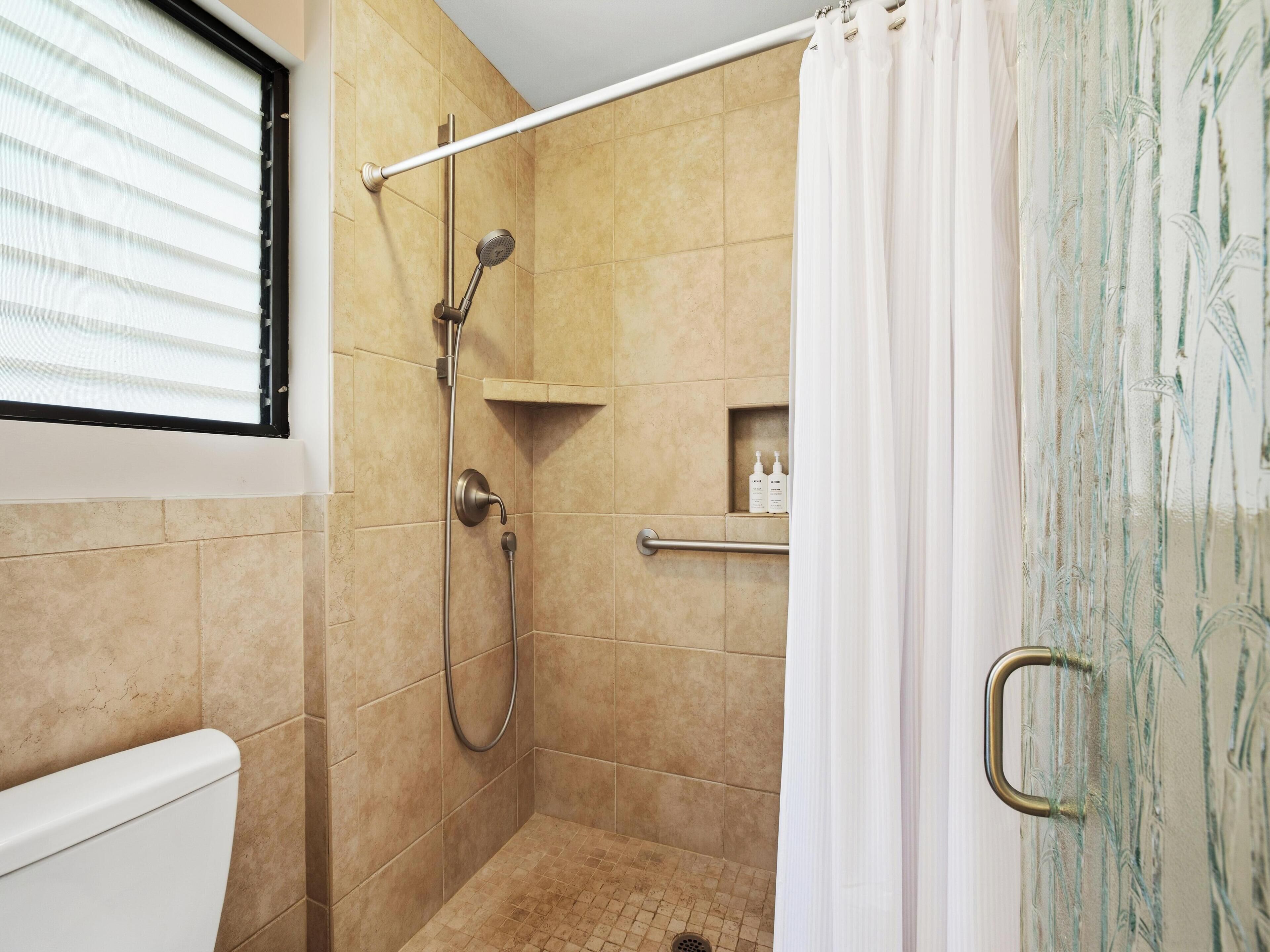 A shower area with a handheld showerhead, a wall-mounted hand shower, and a glass shower door.