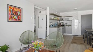 A modern kitchen with white appliances, a dining area with two green chairs, and a 'LOVE LOVE' artwork on the wall.