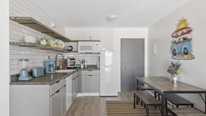 A modern kitchen with white cabinets, a microwave, a refrigerator, and a dining area with a wooden table and benches.