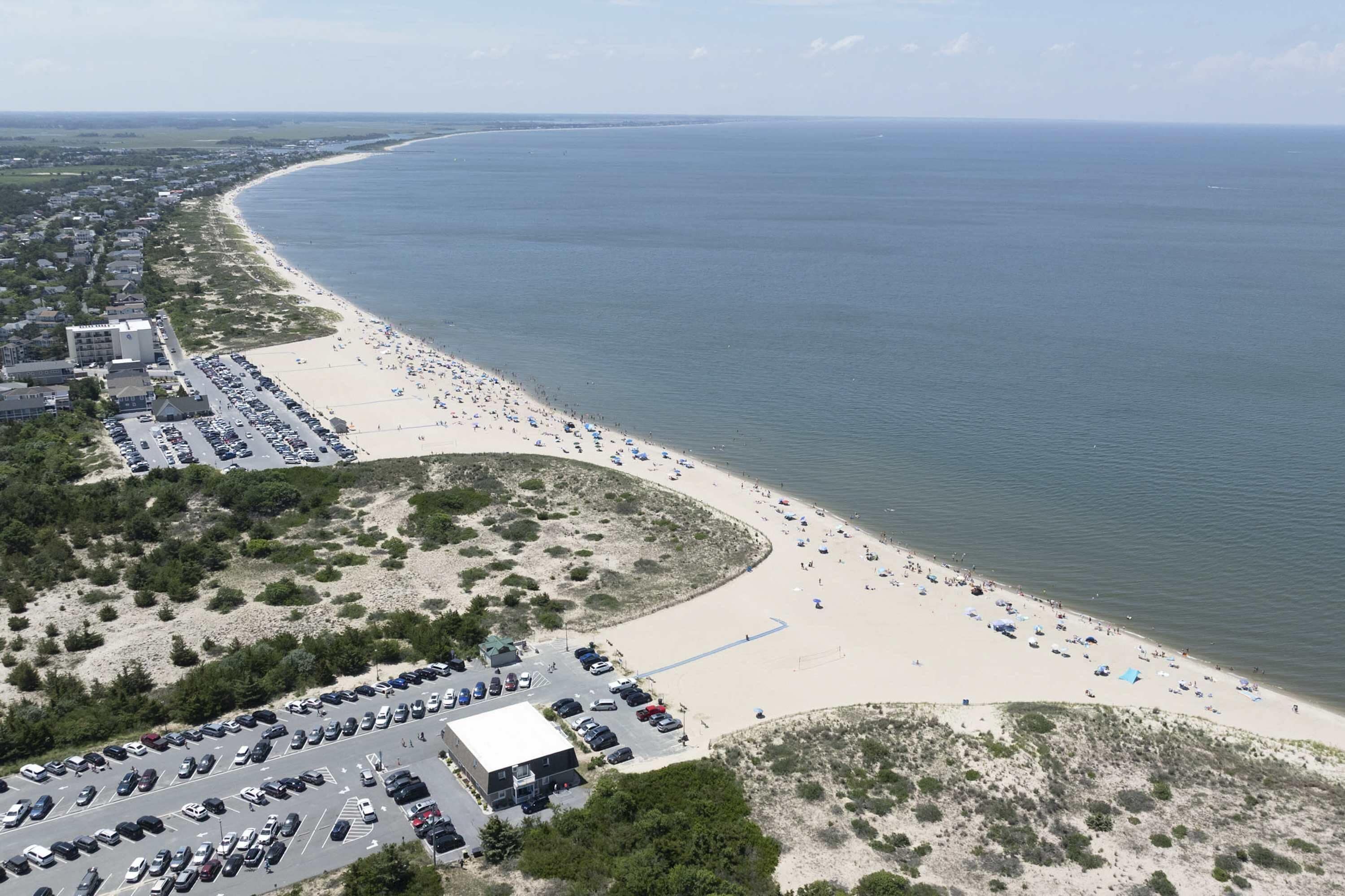 Luchtbeeld van een strand met een parkeerplaats en gebouwen.