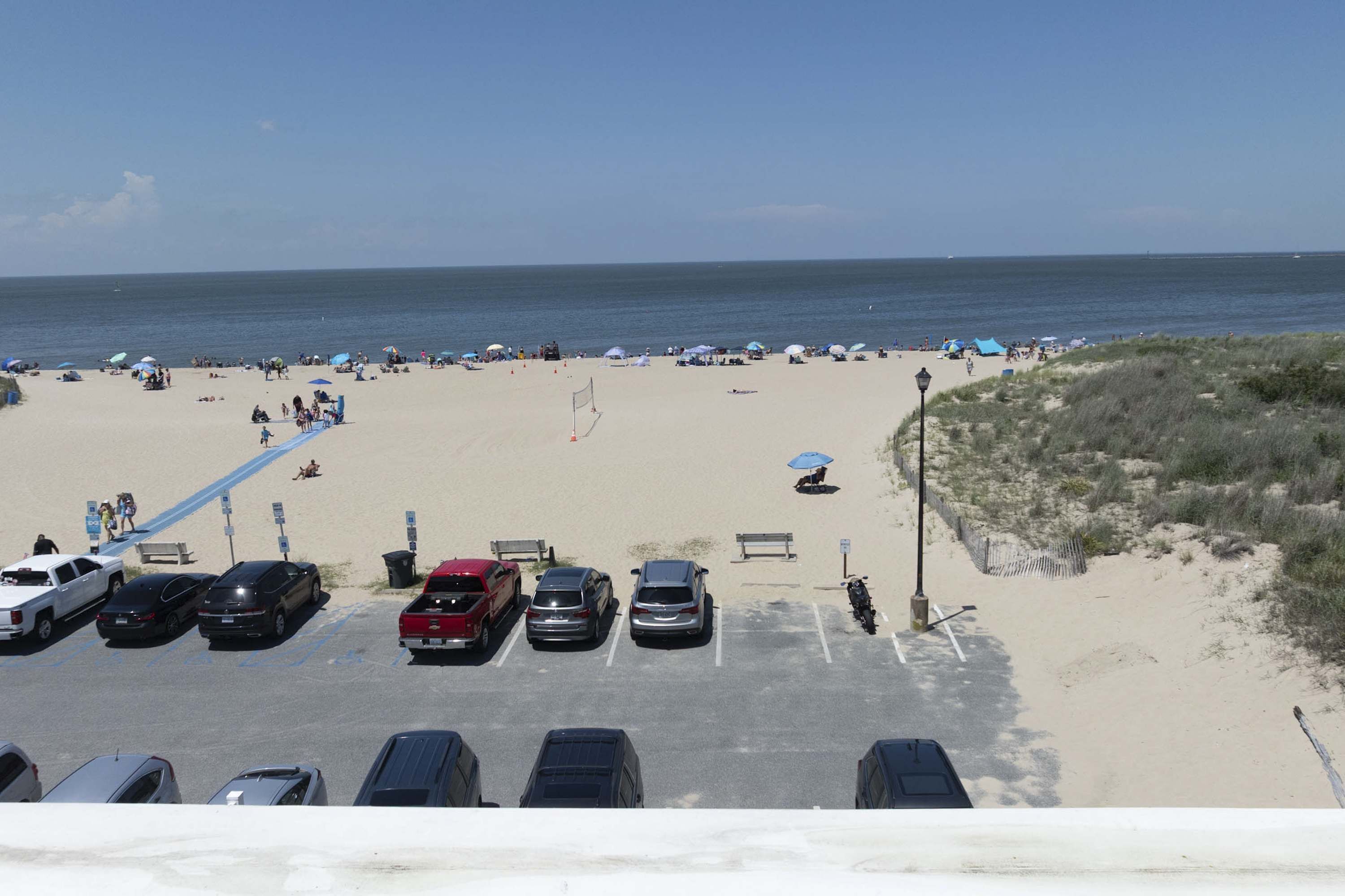A beach with parked cars, umbrellas, and people.