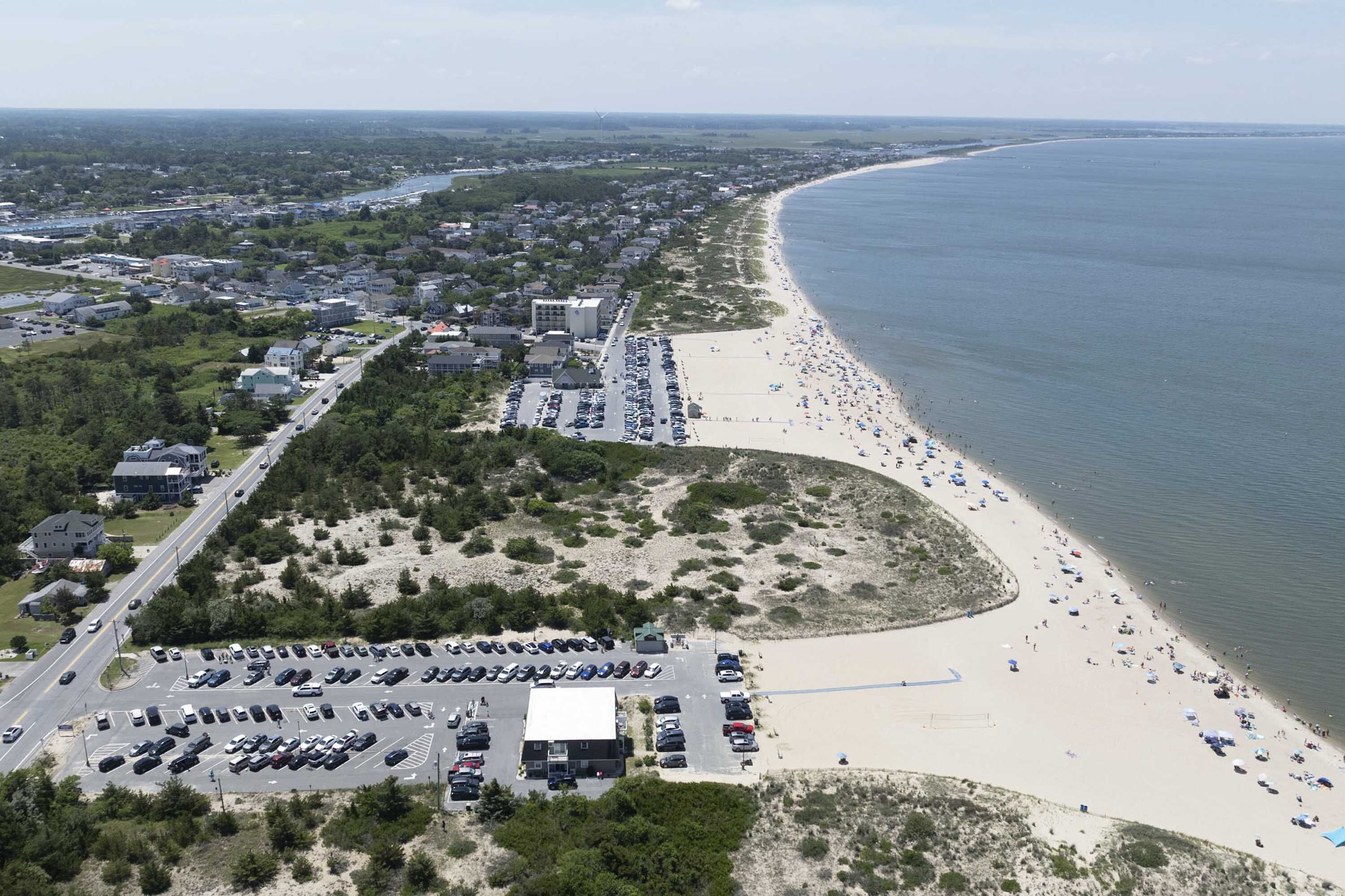 Vue aérienne d’une zone côtière avec une plage, un parking et des bâtiments.