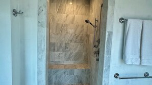 Une salle de bain avec une douche, des murs en marbre, un porte-serviettes et un support à papier toilette.