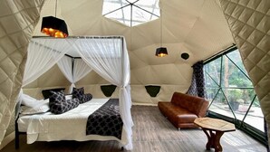 Una habitación tipo tienda de campaña con cama, sofá, una mesita y una ventana.