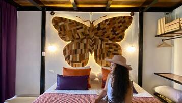A room with a bed, a large wooden butterfly wall art, and a person sitting on the bed.