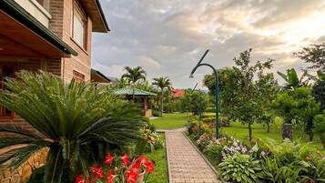 A pathway leading to a building with a brick facade, surrounded by lush greenery and a clear sky.