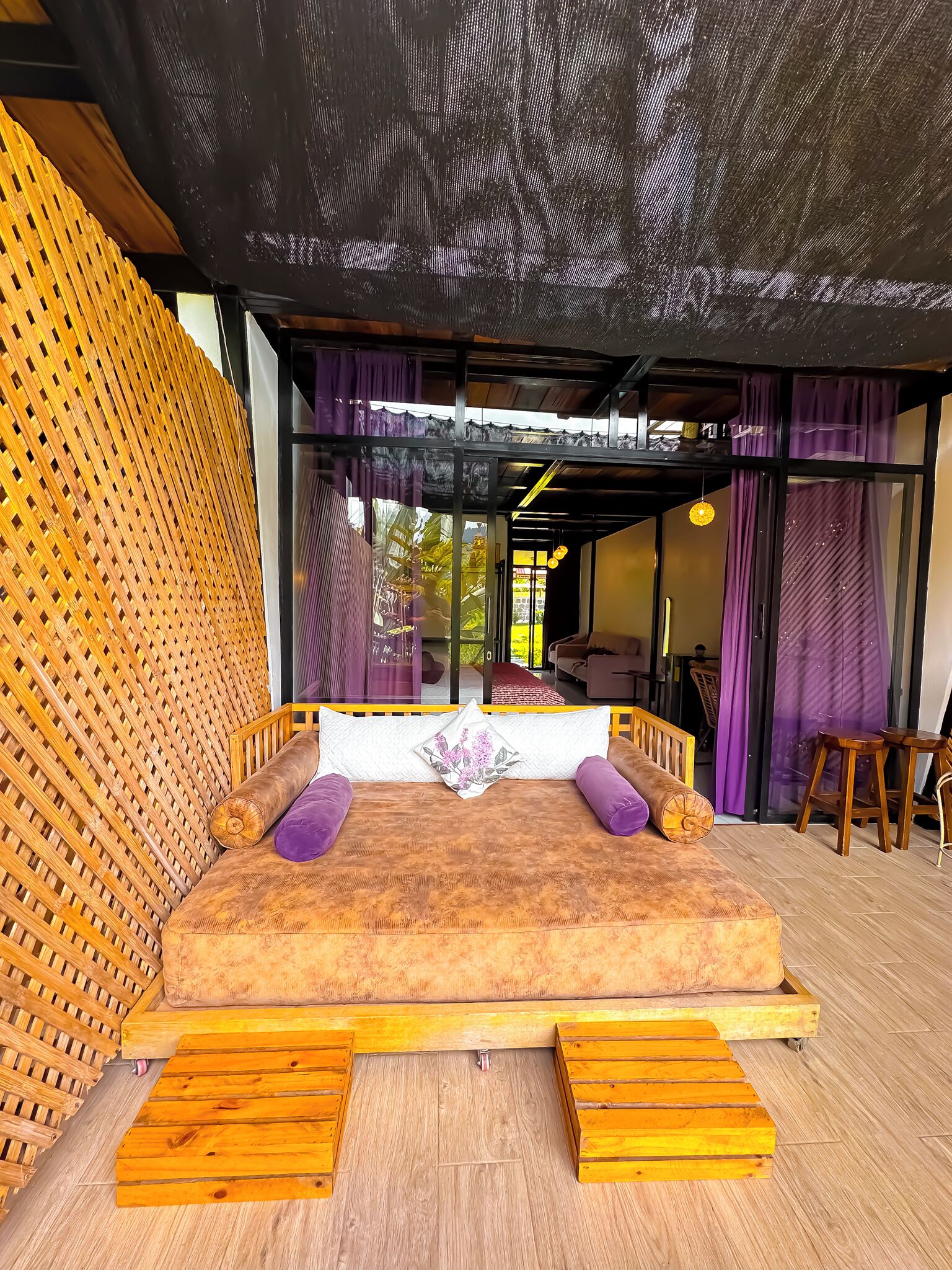 A room with a bed, wooden floor, and a view of the outside.