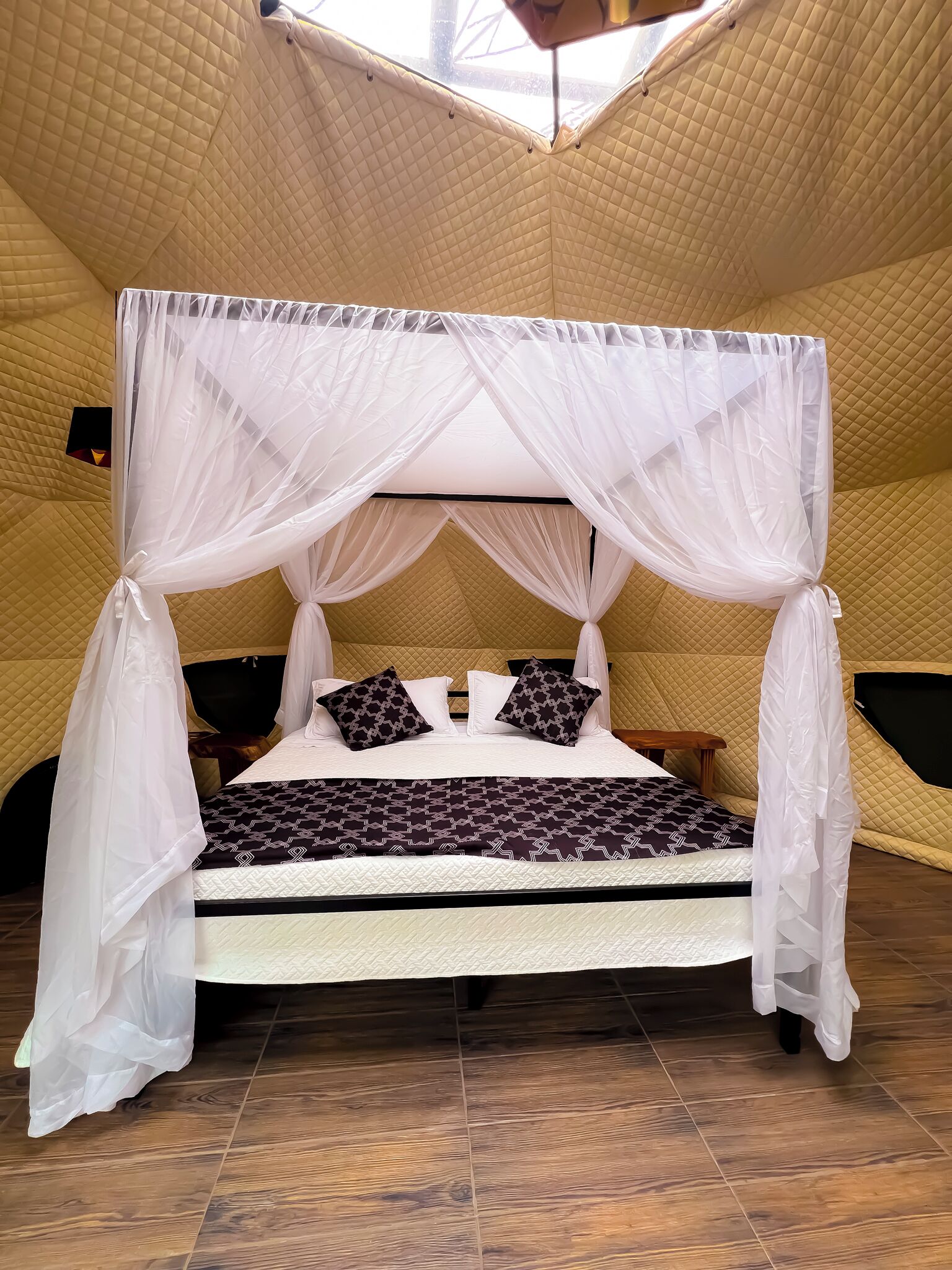 Un lit à baldaquin, doté d’oreillers et d’une couvre-lit à motifs, dans une pièce dont le plafond présente un décor géométrique original.