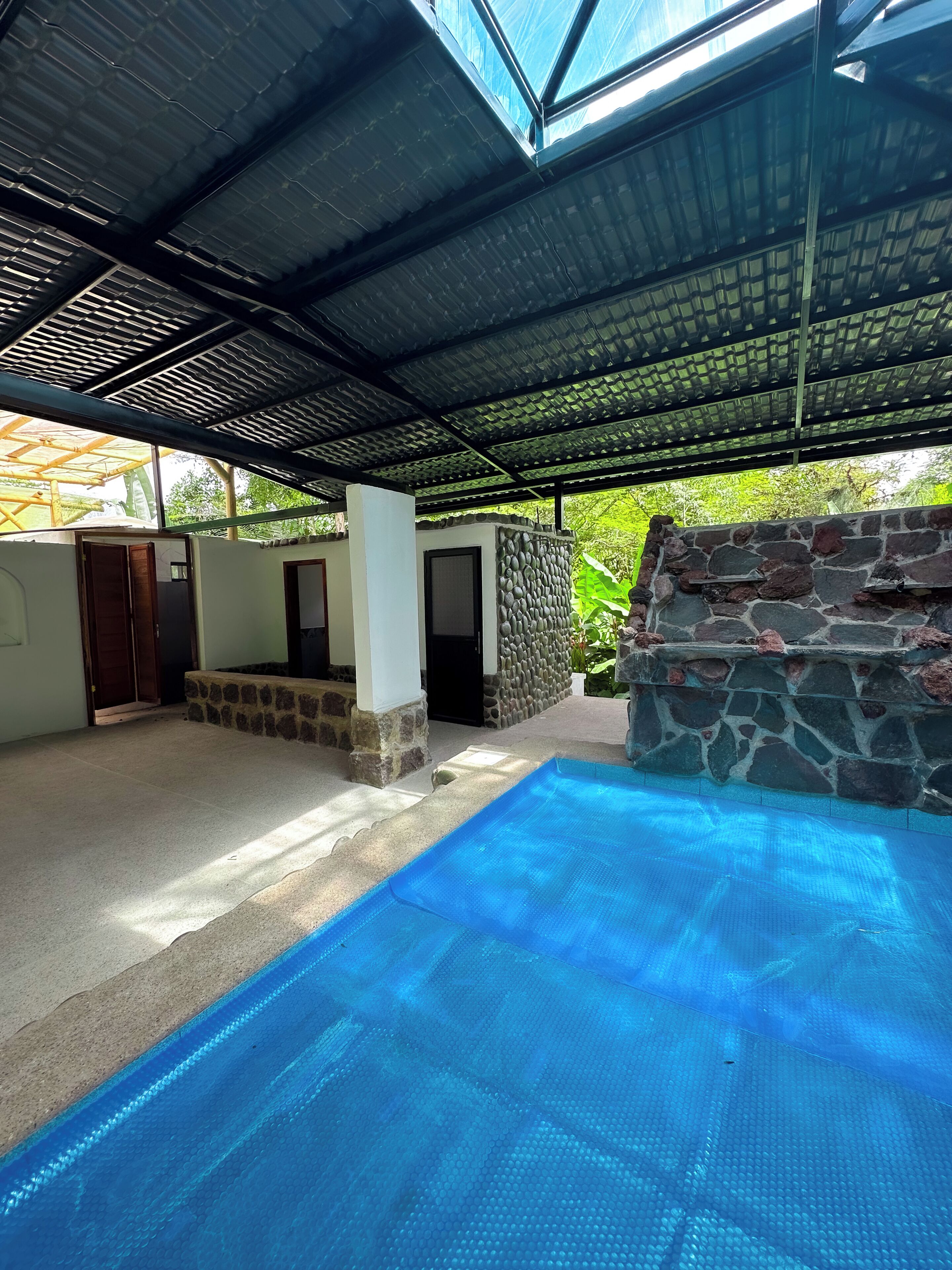 A covered swimming pool area with a stone wall and a glass ceiling.