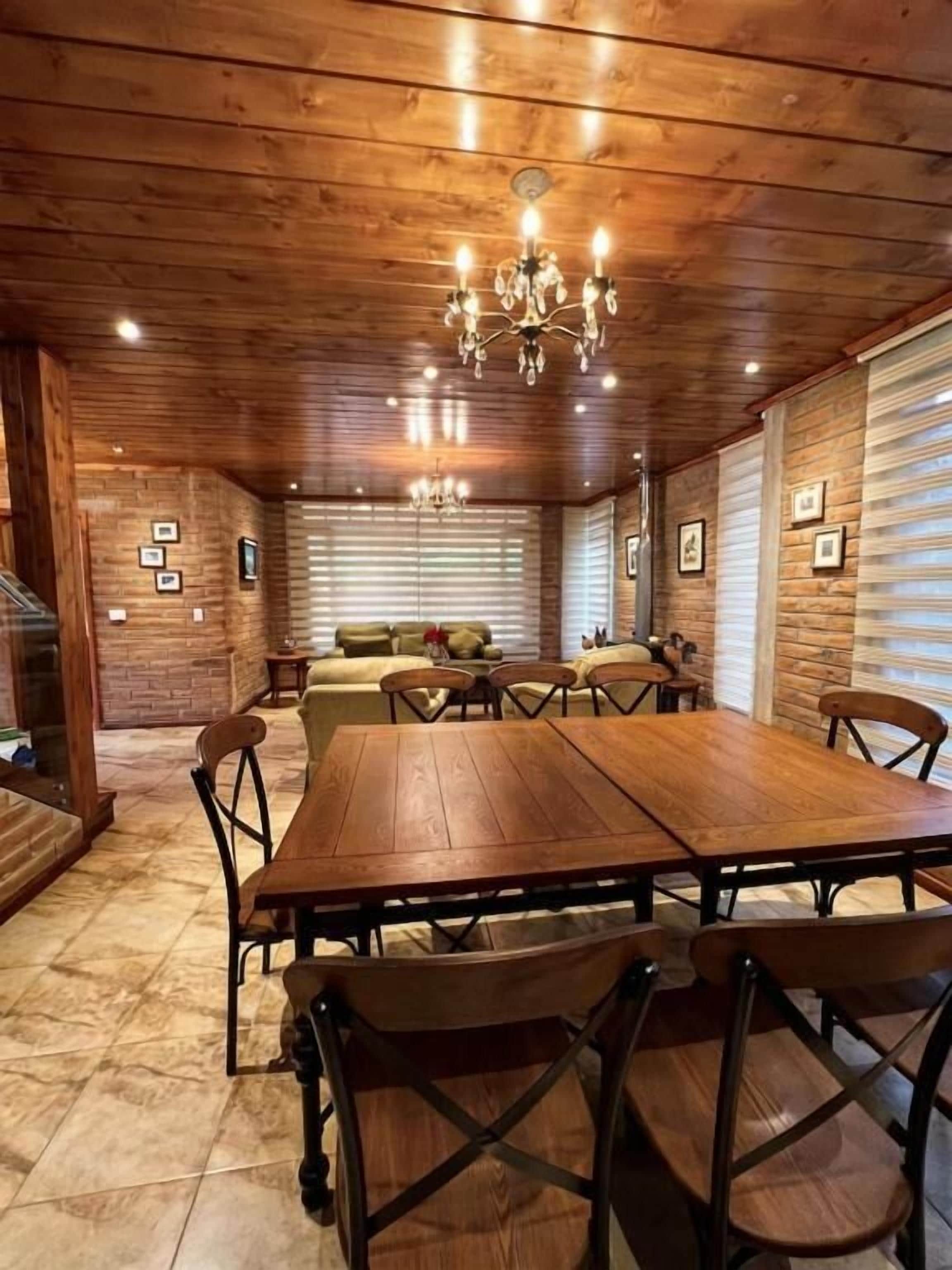Uma área de jantar de madeira com uma mesa grande e cadeiras, um candelabro e quadros nas paredes.