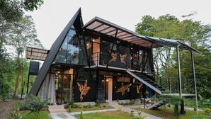 Una casa moderna de dos pisos con fachada de vidrio, una escalera de madera y un jardín con un sendero de piedra.