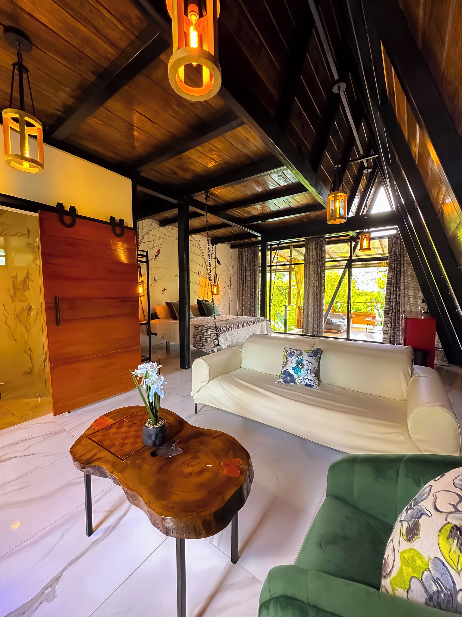 Un loft espacioso con techo alto, un sofá grande, una mesa de centro de madera y vistas al verdor exterior.