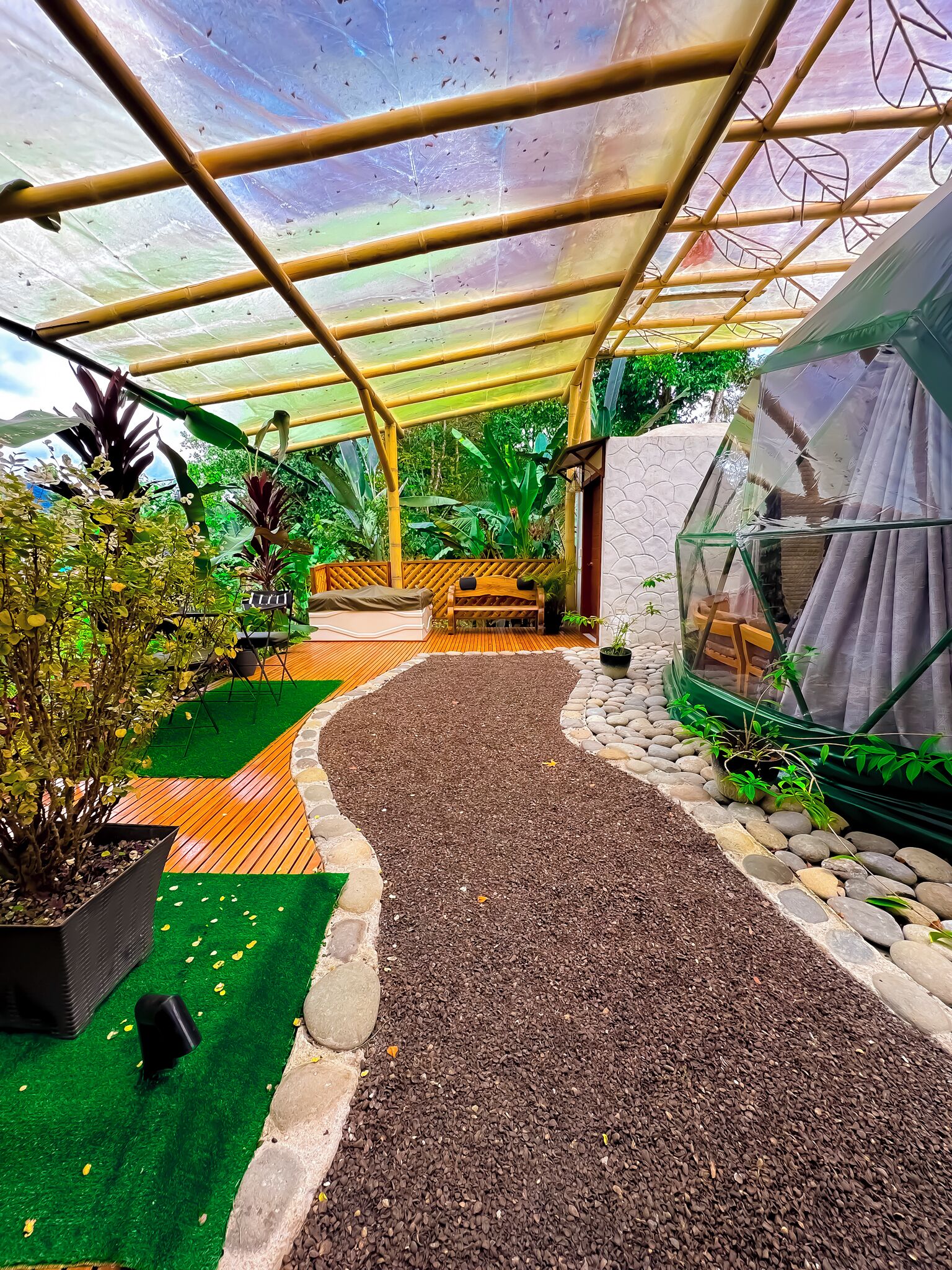 A covered garden area with a gravel path, potted plants, and a wooden bench.