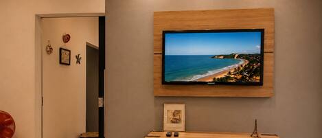 Una sala de estar moderna con un televisor montado, una mesa consola de madera y una puerta que da a otra habitación.
