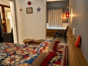Um quarto com uma cama, uma cadeira, uma mesinha e uma janela com cortinas.