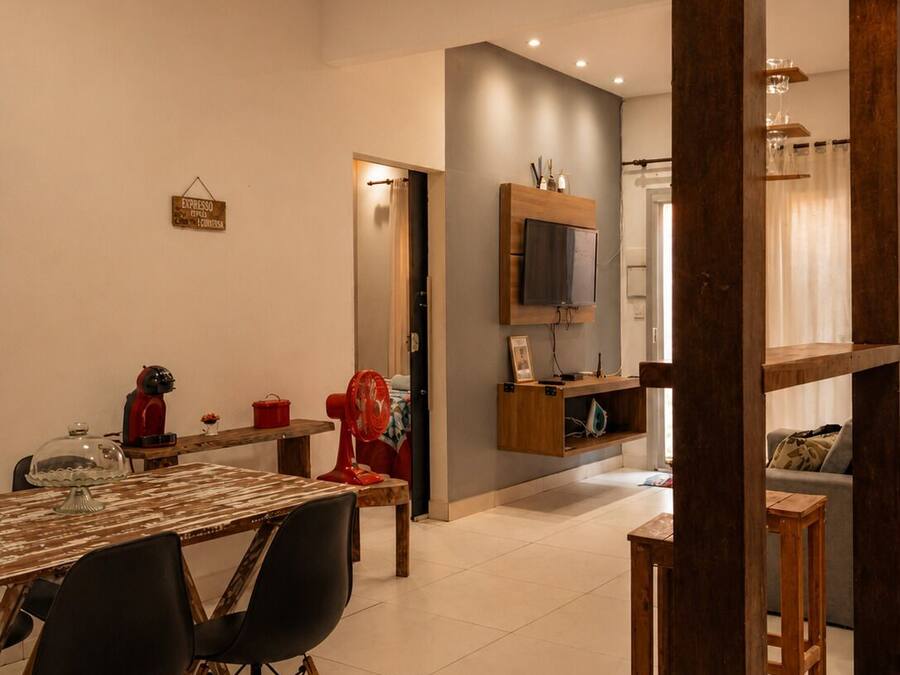A modern living room with a dining area, a TV mounted on the wall, and a wooden ceiling structure.