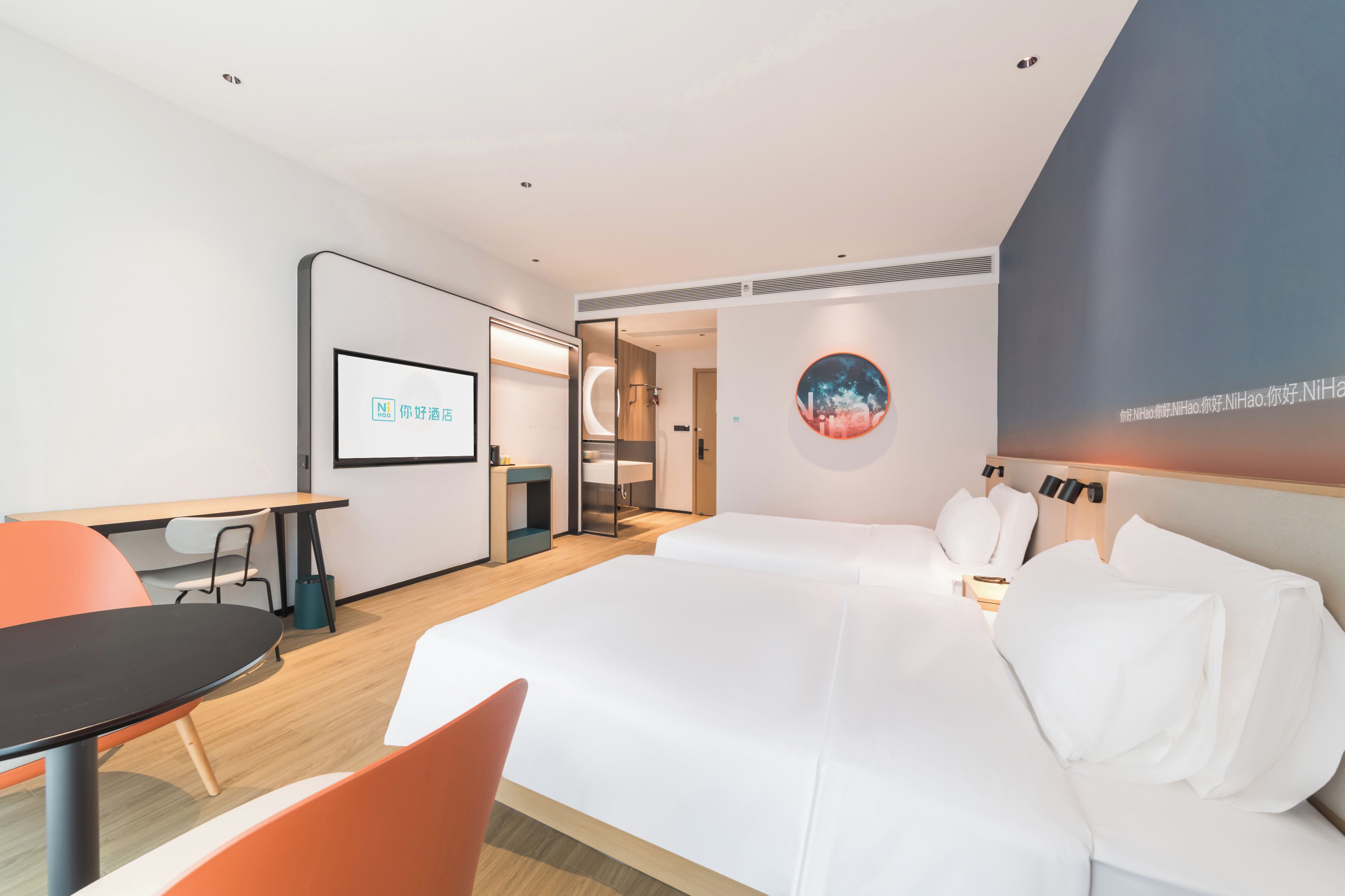 Une chambre d’hôtel comprenant un lit, un bureau, une chaise, un téléviseur et un mur orné d’une œuvre d’art circulaire.