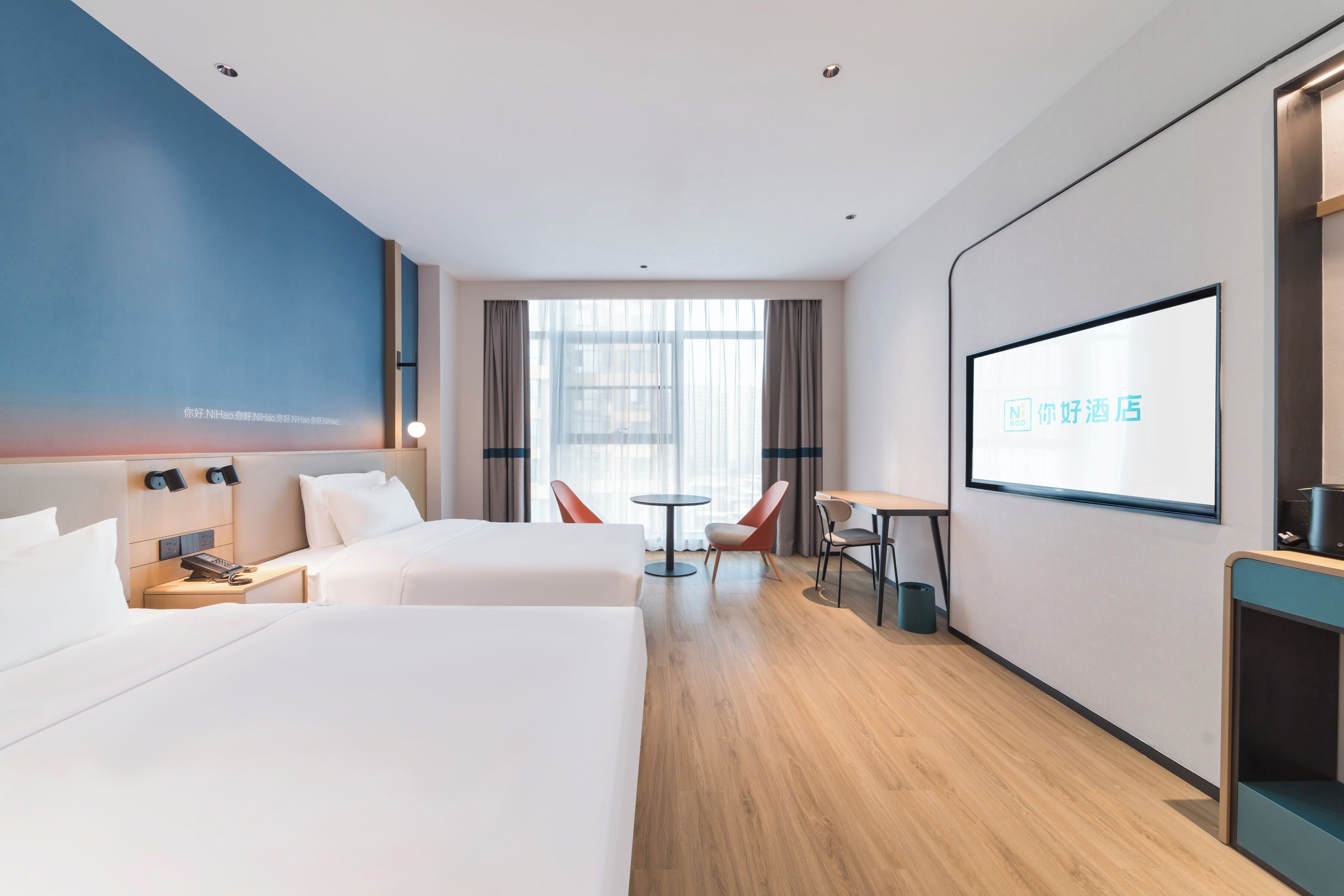 A hotel room with two beds, a desk, a chair, a TV screen, and a large window.
