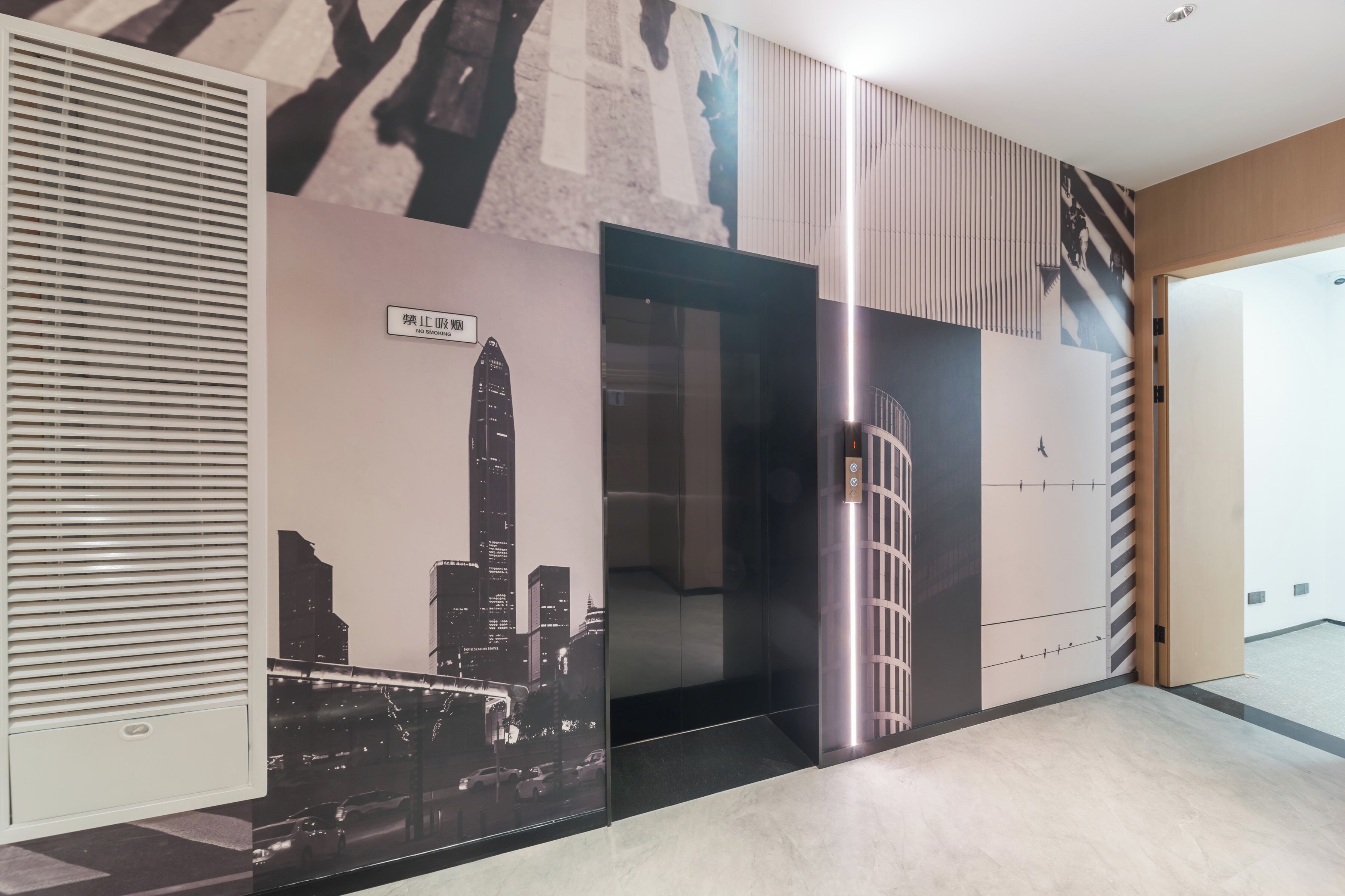 Un ascensor moderno con puerta de vidrio, un mural de paisaje urbano en la pared y una rejilla de ventilación a la izquierda.