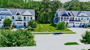 A row of two-story houses with a well-maintained lawn and a white fence in the foreground. - New Coastal Club Luxury Villa w Resort style Amenities | Sleeps 8 | 3BR / 2.5 Baths (Lewes)