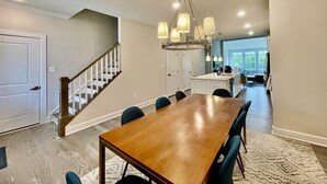 A spacious dining area with a wooden table and chairs, a chandelier, and a view into the kitchen. - New Coastal Club Luxury Villa w Resort style Amenities | Sleeps 8 | 3BR / 2.5 Baths (Lewes)