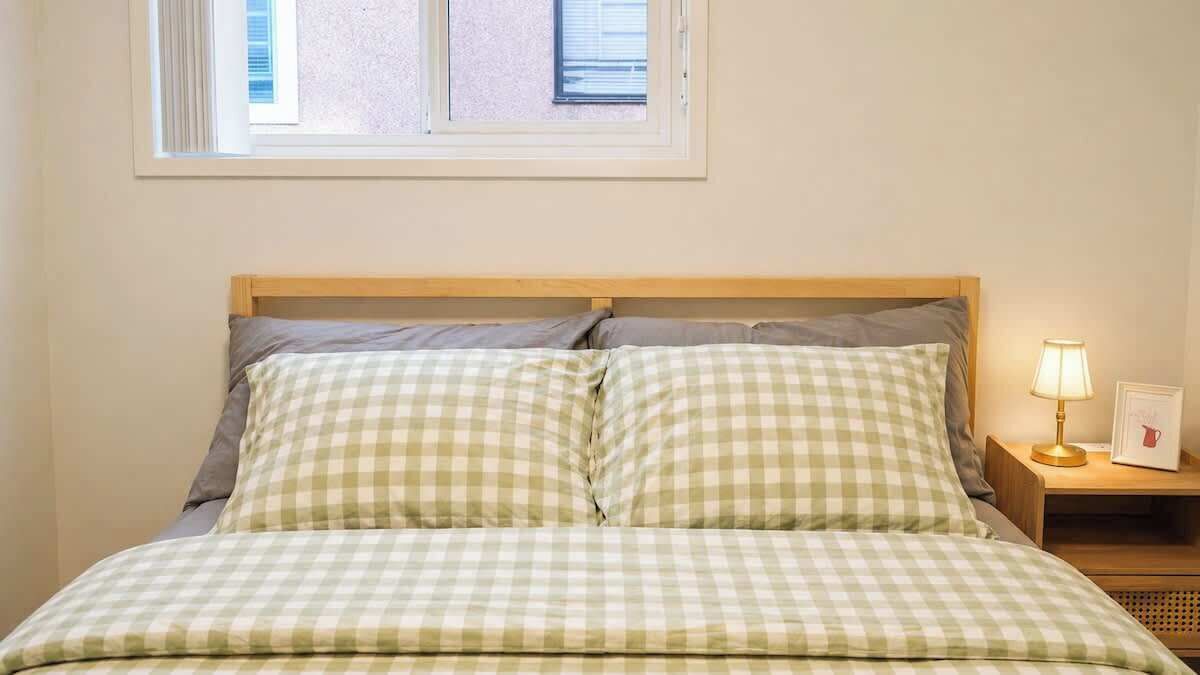 A bed with checkered bedding, a nightstand with a lamp, and a window above the bed.