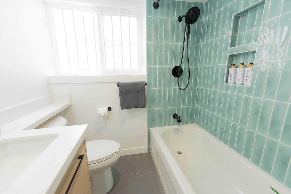 A bathroom with a white toilet, a bathtub, and a window with bars.