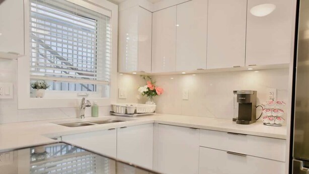 A modern kitchen with white cabinets, a stainless steel refrigerator, a coffee machine, and a window with blinds. - Private 3Bed Entire House/ 15 mins YVR/ 20 mins DT (Vancouver)