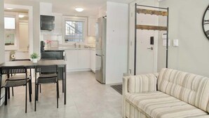 A modern kitchen with white cabinets, a dining table with chairs, a sofa, and a large wall clock. - Private 3Bed Entire House/ 15 mins YVR/ 20 mins DT (Vancouver)