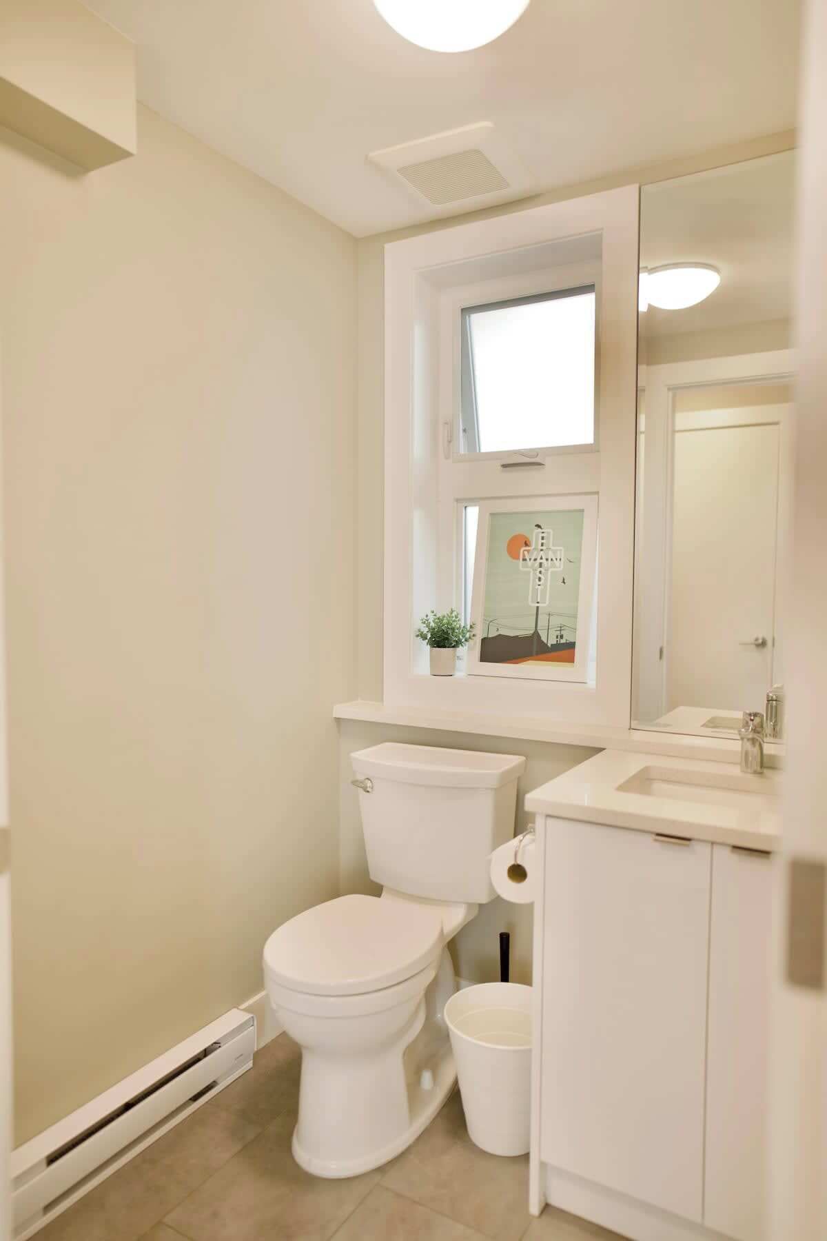Un baño con inodoro, lavabo y ventana sobre el inodoro.