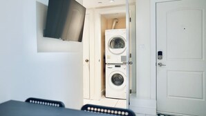 Una habitación compacta con lavadora, televisor montado en la pared y una puerta.