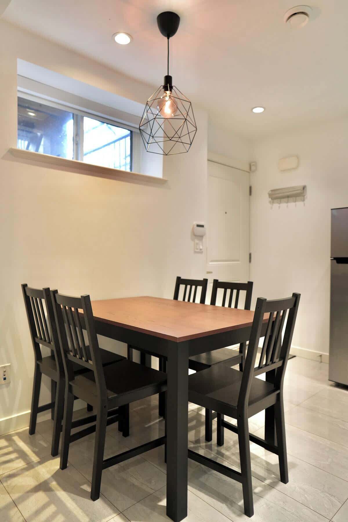 A dining area with a wooden table and chairs, a pendant light, and a window.