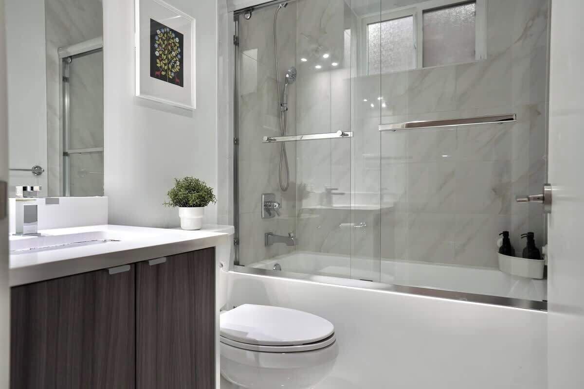 Et moderne badeværelse med en brusekabine i glas, et hvidt toilet og en vask med en plante.