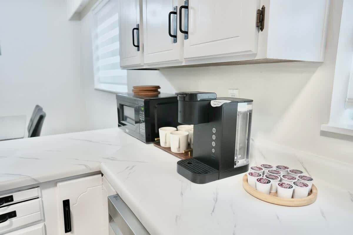 Une cuisine avec des meubles blancs, un four à micro-ondes, une machine à café et un plateau de dosettes de café.